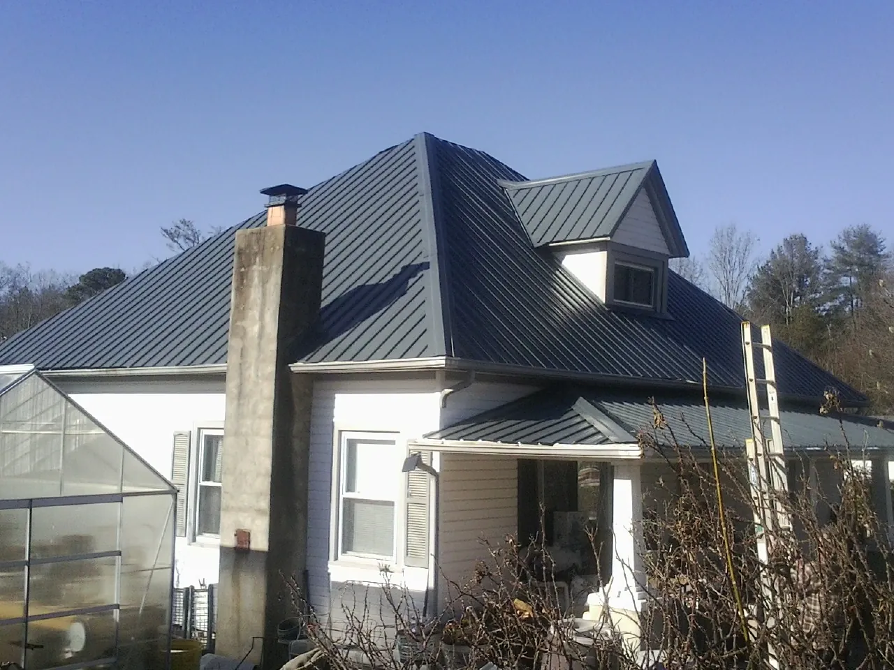 Dark blue standing seam metal roof on a white farmhouse with dormer — Slate & Tile Roof Repair by Roofing Brothers in Minnetonka