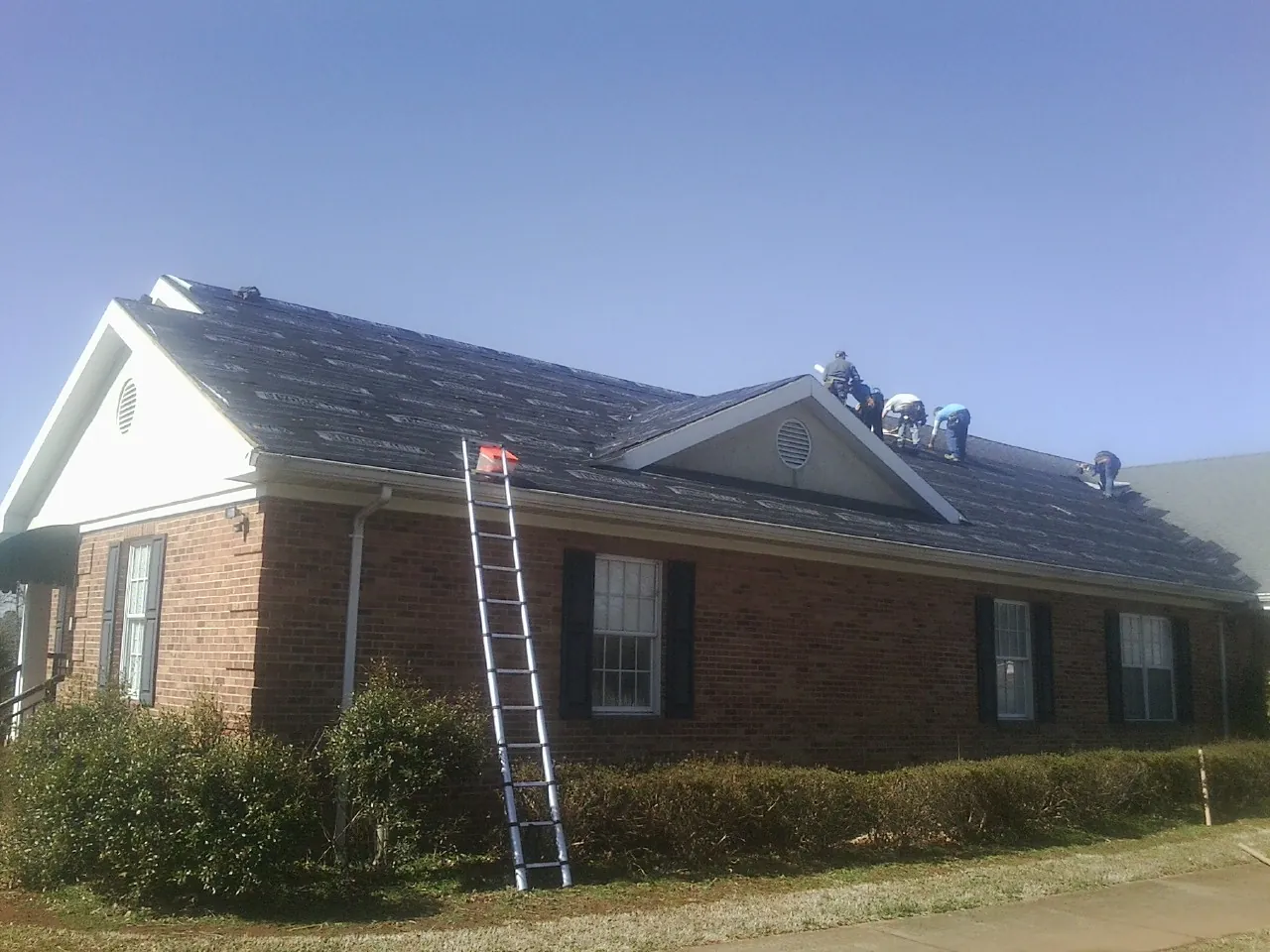 Crew tearing shingles off a brick ranch roof with a ladder set — Emergency Roof Repair work by our crew in Minnetonka