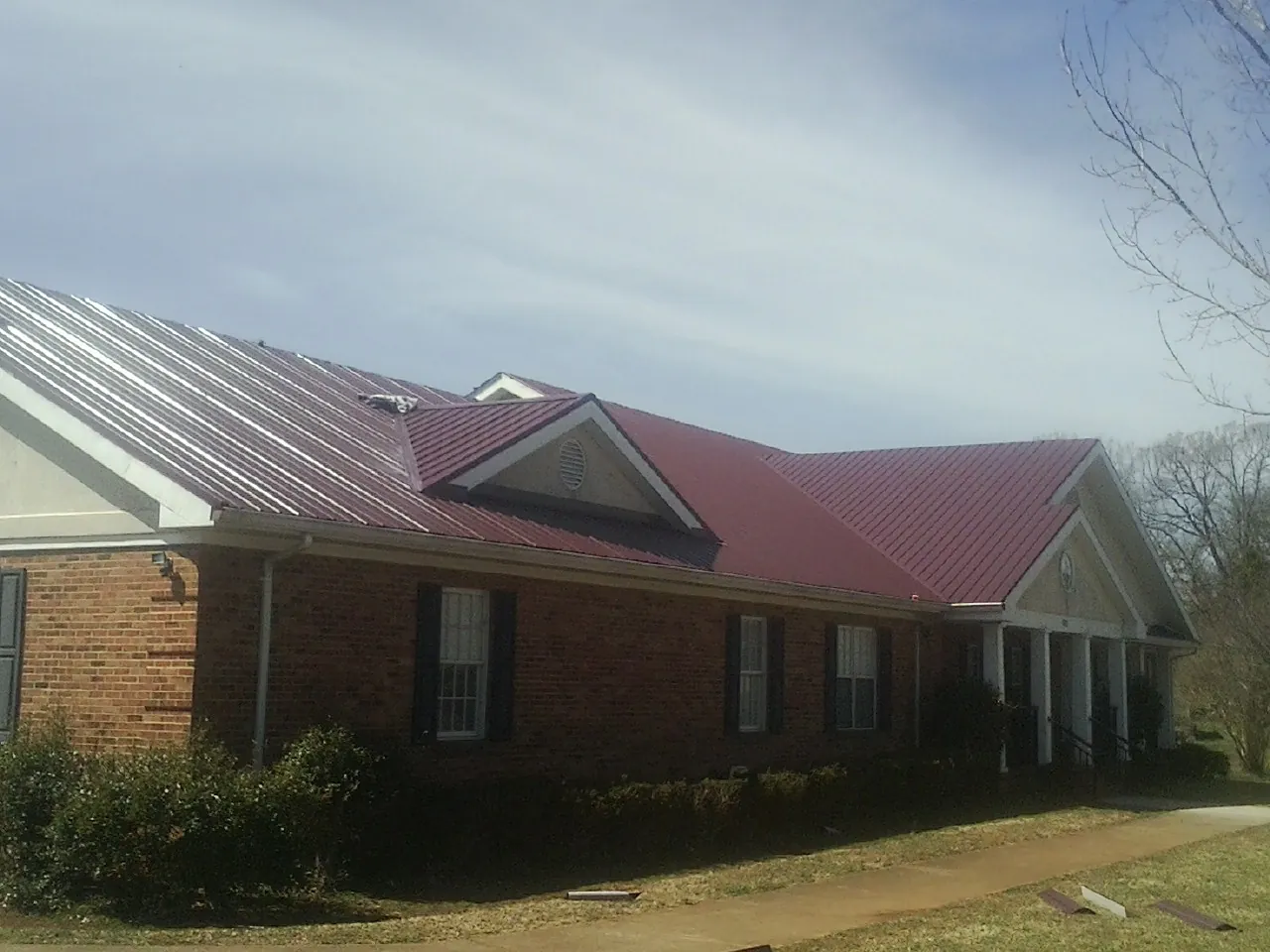 Red metal roof with gabled entries on a long brick building, from a Hail Damage Roof Repair job in Minnetonka