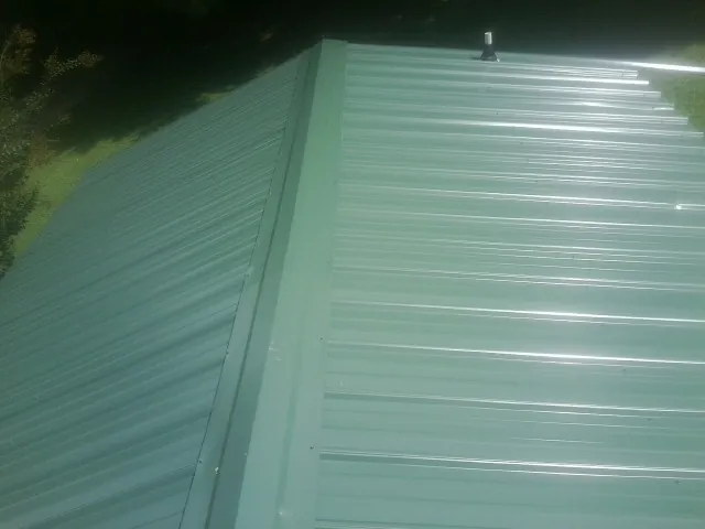 New green metal panels meeting at the ridge of a roof — Flat Roof Repair work by our crew in Minnetonka
